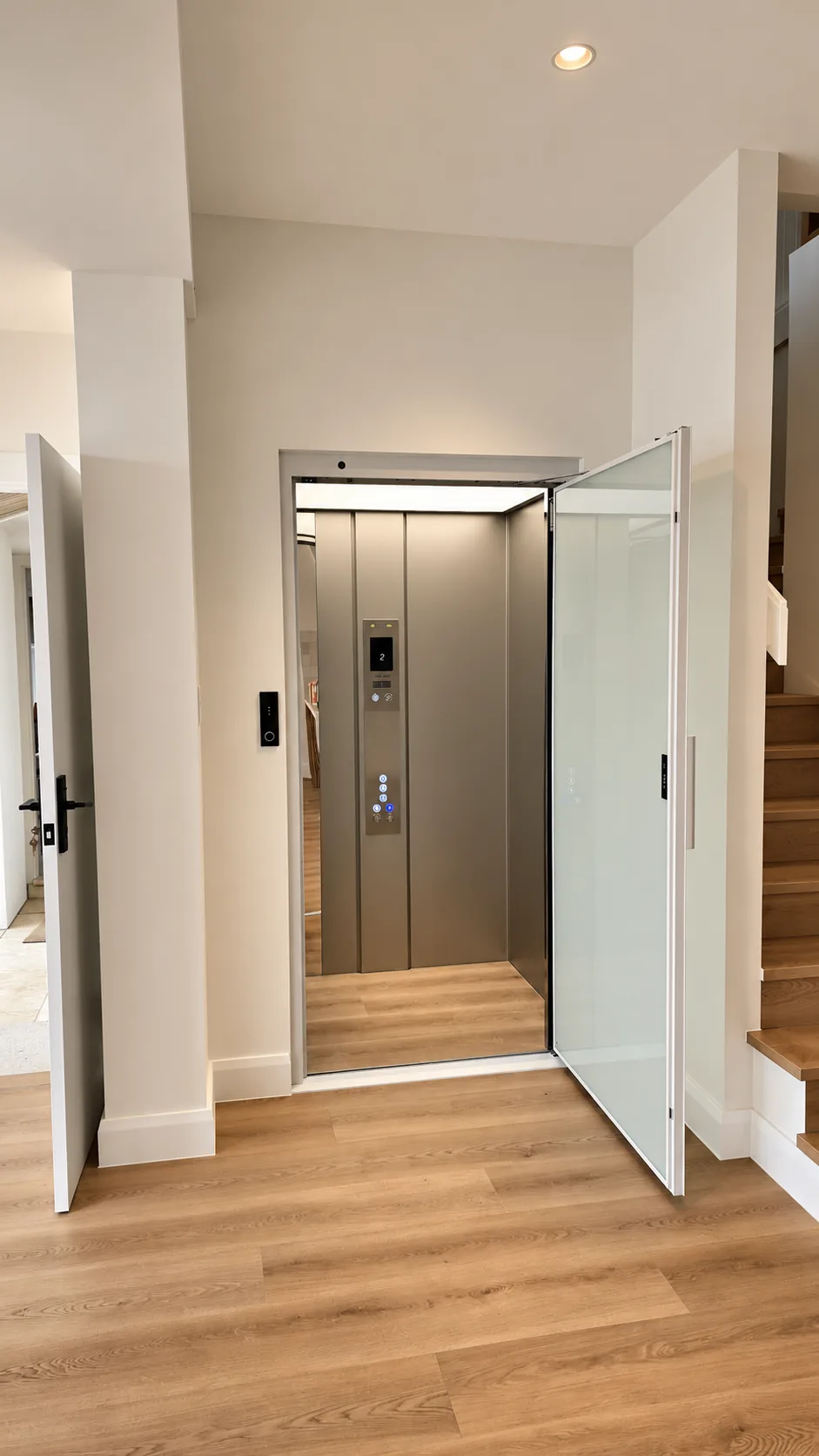 The private internal lift serving three levels of the Terrigal residence, its glass-panelled door open, showing a bronze-toned cabin with a control panel and timber-look floor, beside the staircase